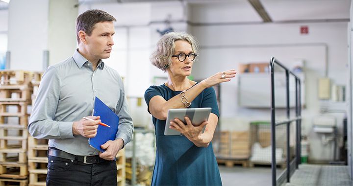 Two business people working in a warehouse with a tablet device and holding a folder