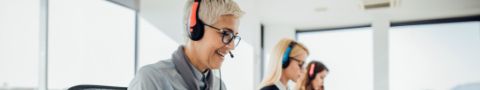 Three people wearing headsets work in an office. 