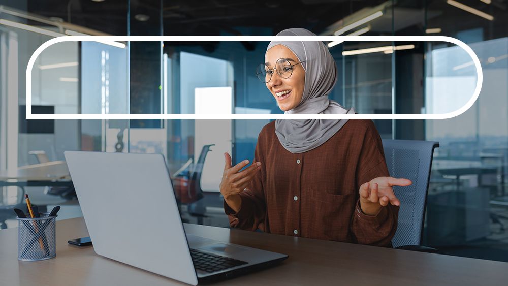 Woman smiling at open computer laptop engaging in Zoom chat at her desk. 