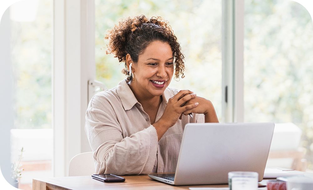 Woman smiling at an open computer laptop engaging in Zoom chat at her desk. 